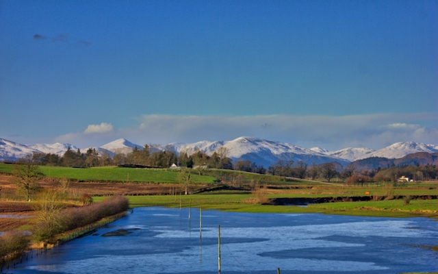 A blue sky with white topped mountains and a flooded field in front
