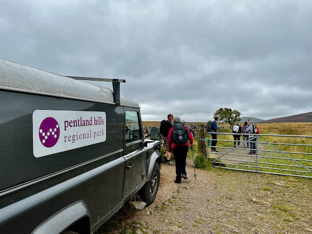 A Pentlandite Hills Regional Park Landrover by a gate through which a walking group is passing.