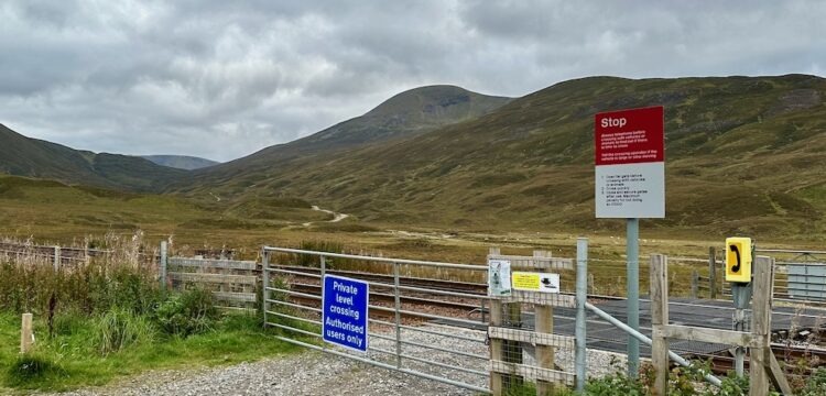 A storm sky, mountains and a level crossing with track and warning signs.