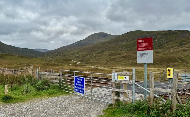 A storm sky, mountains and a level crossing with track and warning signs.